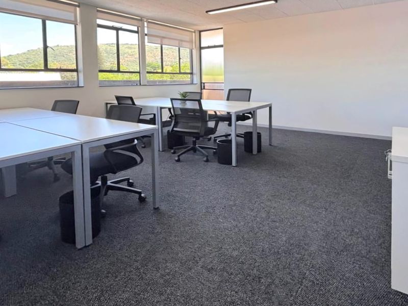 A bright, open-plan commercial office space featuring large windows, neutral carpeting, and a clean, professional layout suitable for a modern workspace.