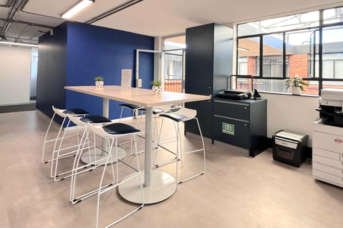 A modern commercial office breakout area featuring a high-top table, built-in storage cabinetry, and large windows providing natural light.