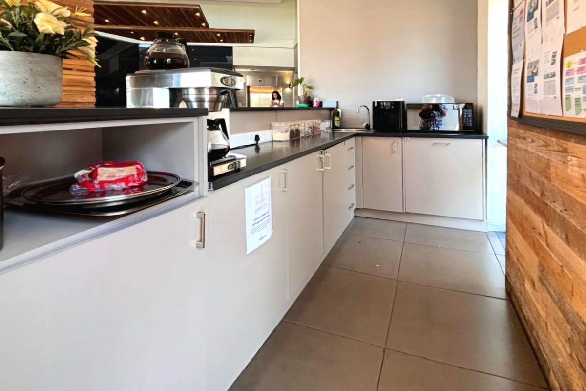 A functional kitchenette area featuring built-in cabinetry, laminate countertops, a stainless steel sink, and modern tiled flooring with decorative timber wall paneling.