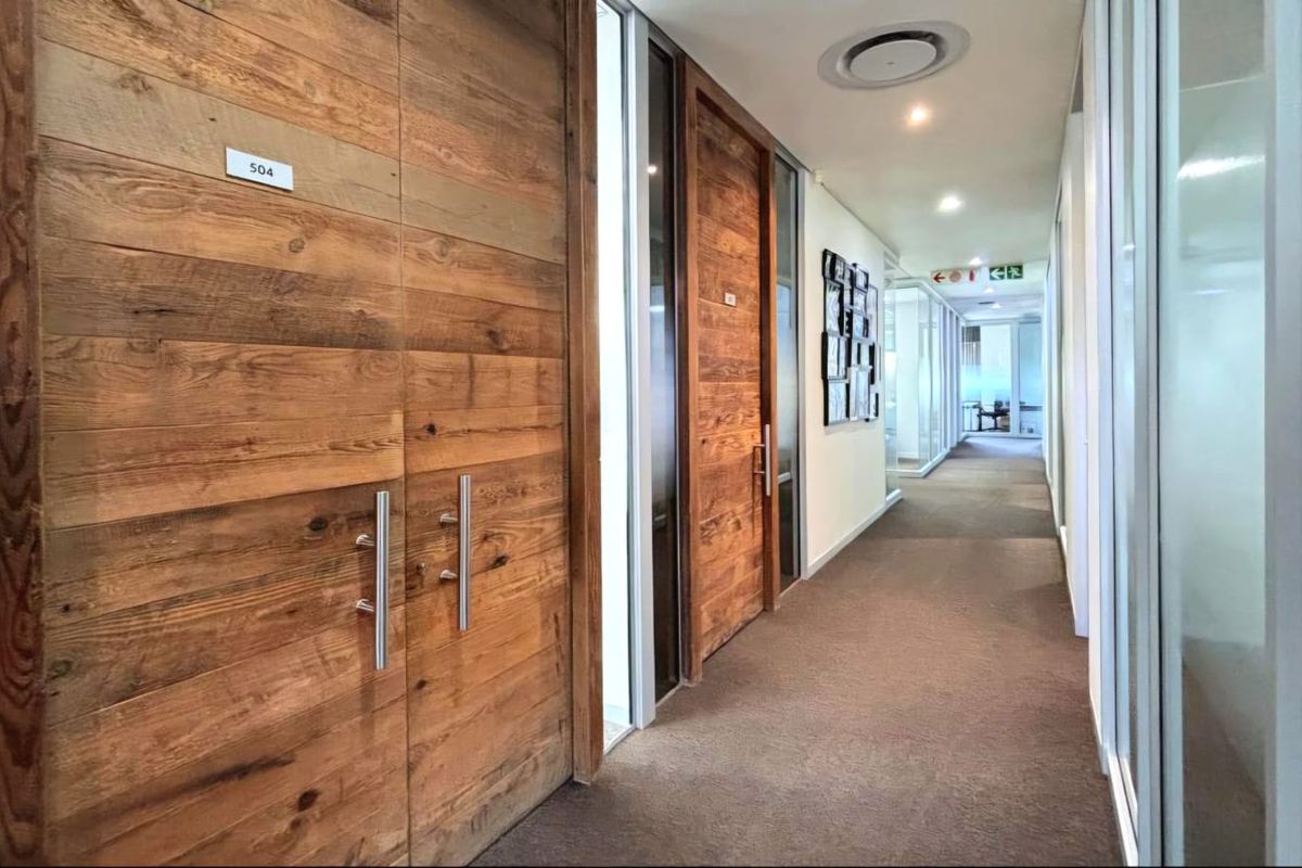 A professional commercial office hallway featuring timber-clad doors, glass partitions, and recessed ceiling lighting, creating a modern and clean workspace environment.