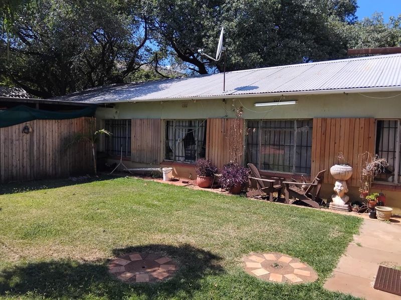 Rear view of the farm property featuring a corrugated metal roof, security-barred windows, and wooden privacy screening overlooking a private lawn area.
