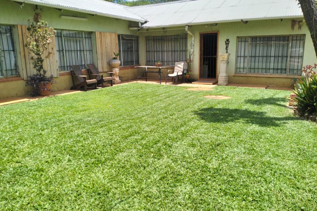 Rear view of the farmhouse featuring a well-maintained lawn, concrete patio area, and corrugated metal roofing with security bars on windows.