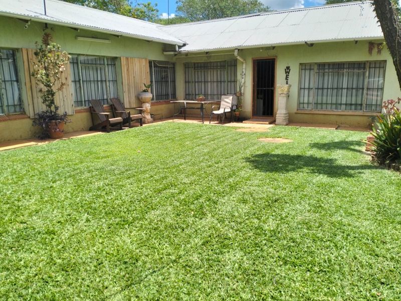 Rear view of the farmhouse featuring a well-maintained lawn, concrete patio area, and corrugated metal roofing with security bars on windows.