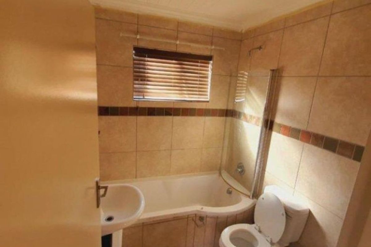 A functional bathroom featuring a corner bathtub with a glass screen, pedestal basin, and toilet, finished with neutral wall and floor tiling.