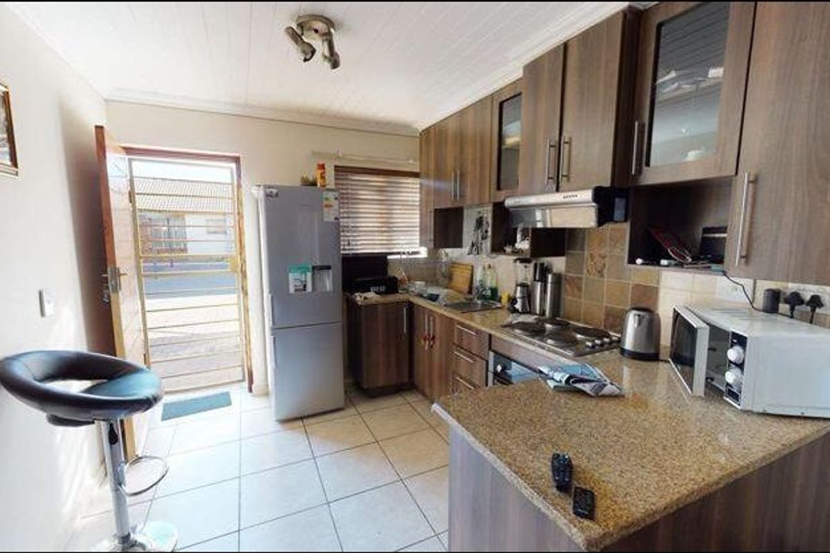 Functional kitchen featuring granite countertops, built-in cabinetry, and integrated appliances, with direct access to the exterior via a security gate.