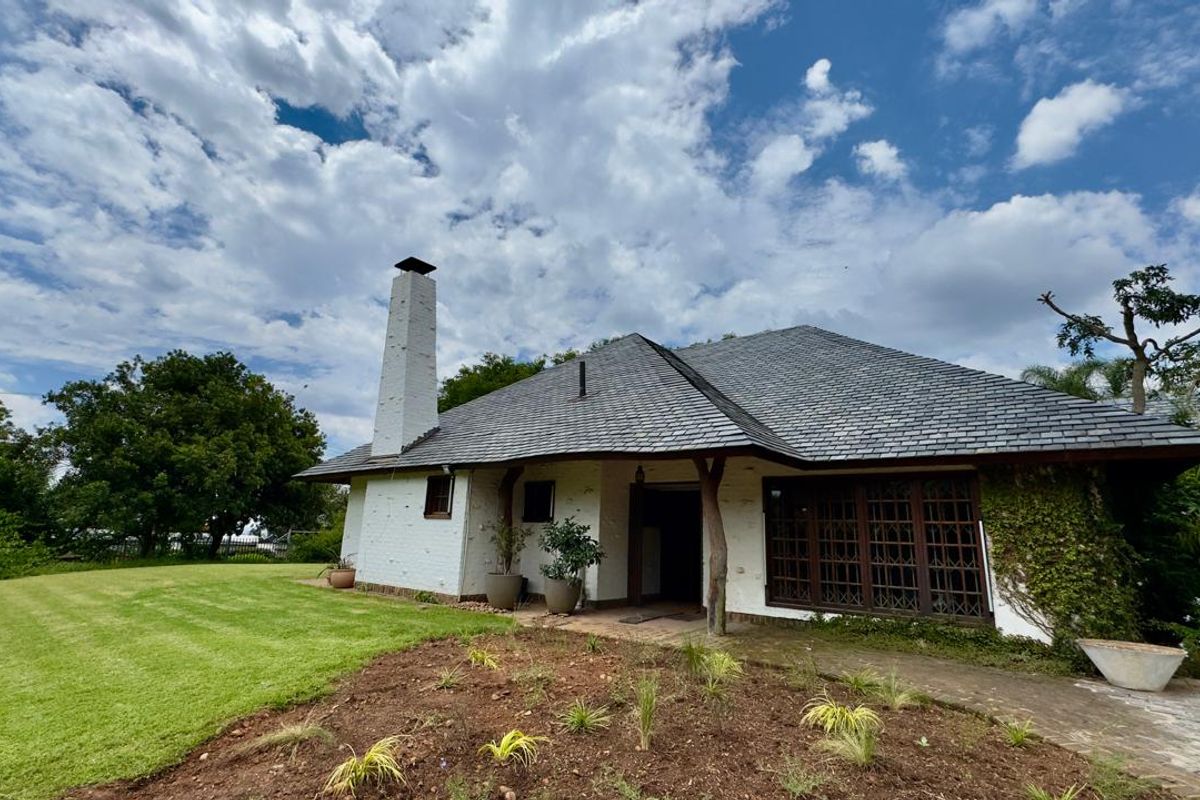 A rear view of a white brick house featuring a prominent chimney, slate roof, and large timber-framed windows overlooking a spacious garden.