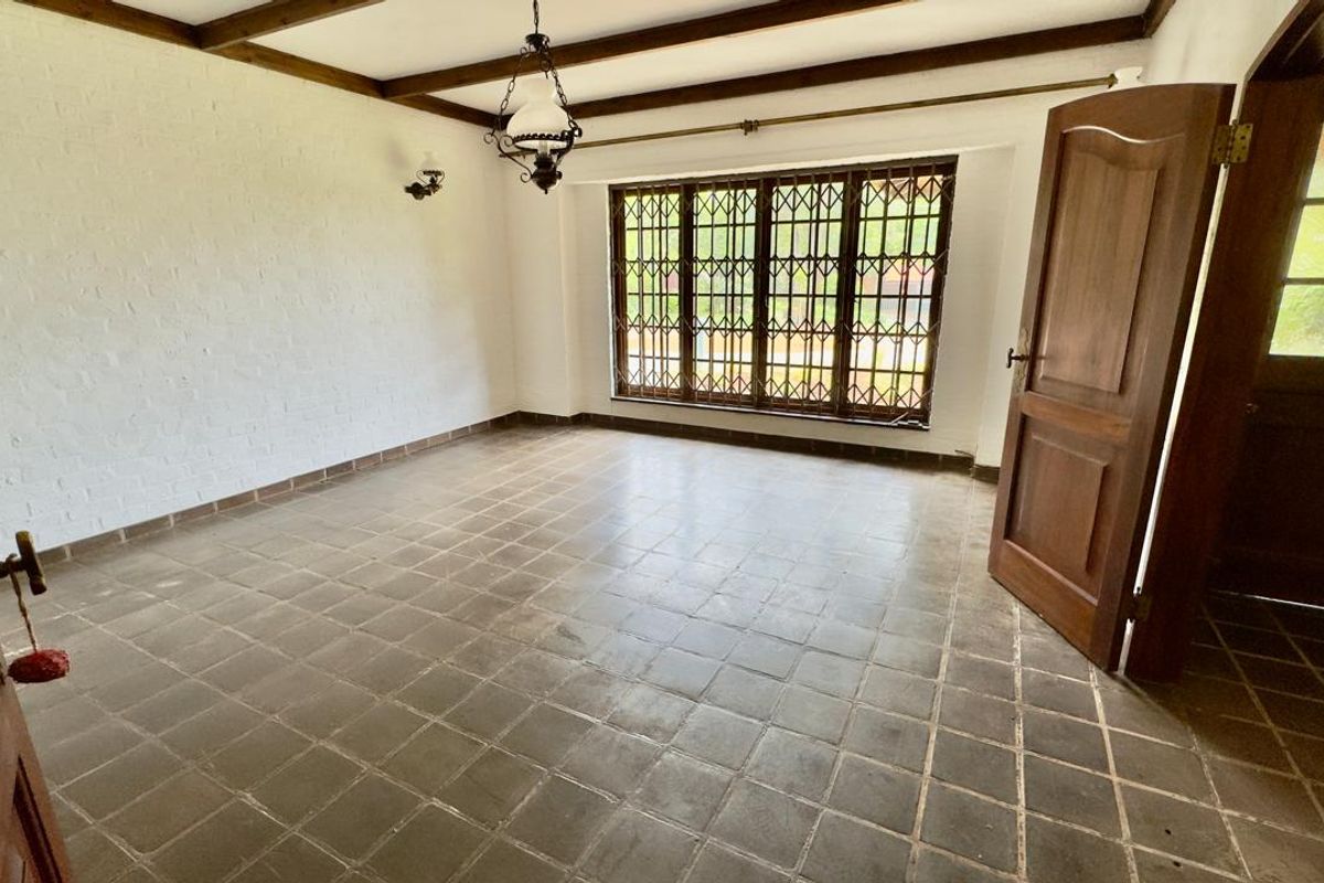 An empty living room featuring exposed timber ceiling beams, tiled flooring, and a large window with security bars.