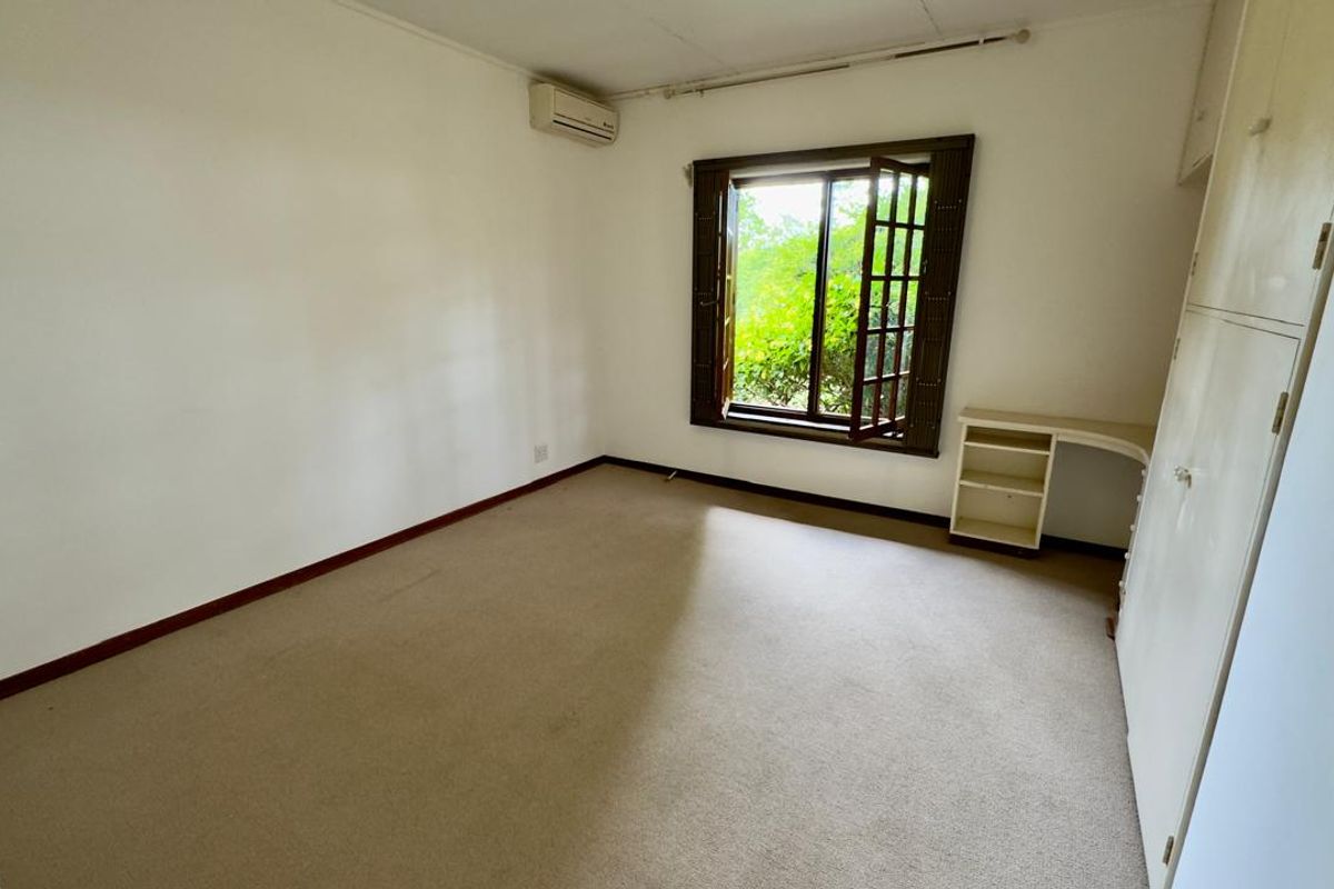 A vacant bedroom featuring neutral carpeting, built-in storage cabinetry, a wall-mounted air conditioning unit, and a window overlooking greenery.