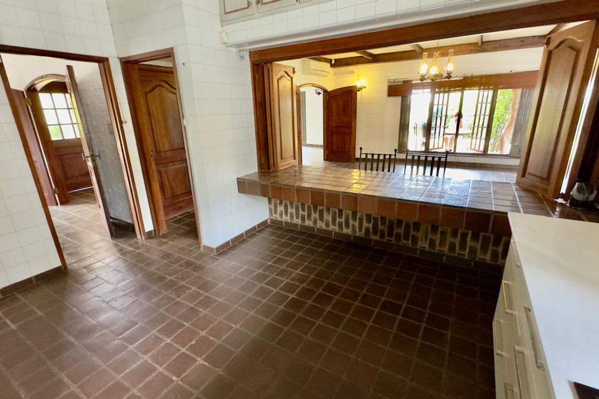 A kitchen area featuring a tiled breakfast bar, terracotta-style floor tiles, and wooden door frames, connecting to an adjacent living space.