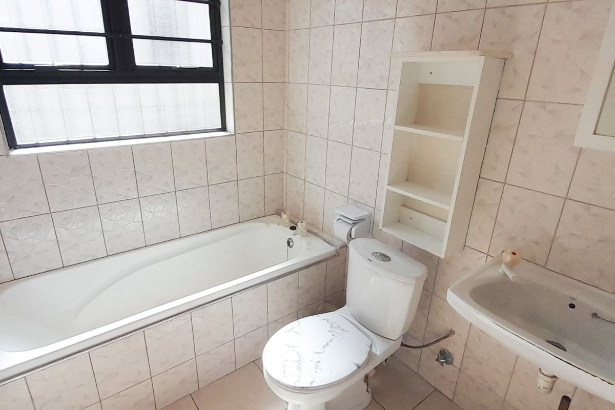 A functional bathroom featuring a bathtub, toilet, and wall-mounted basin with fully tiled walls and floor, offering a blank canvas for modernization.