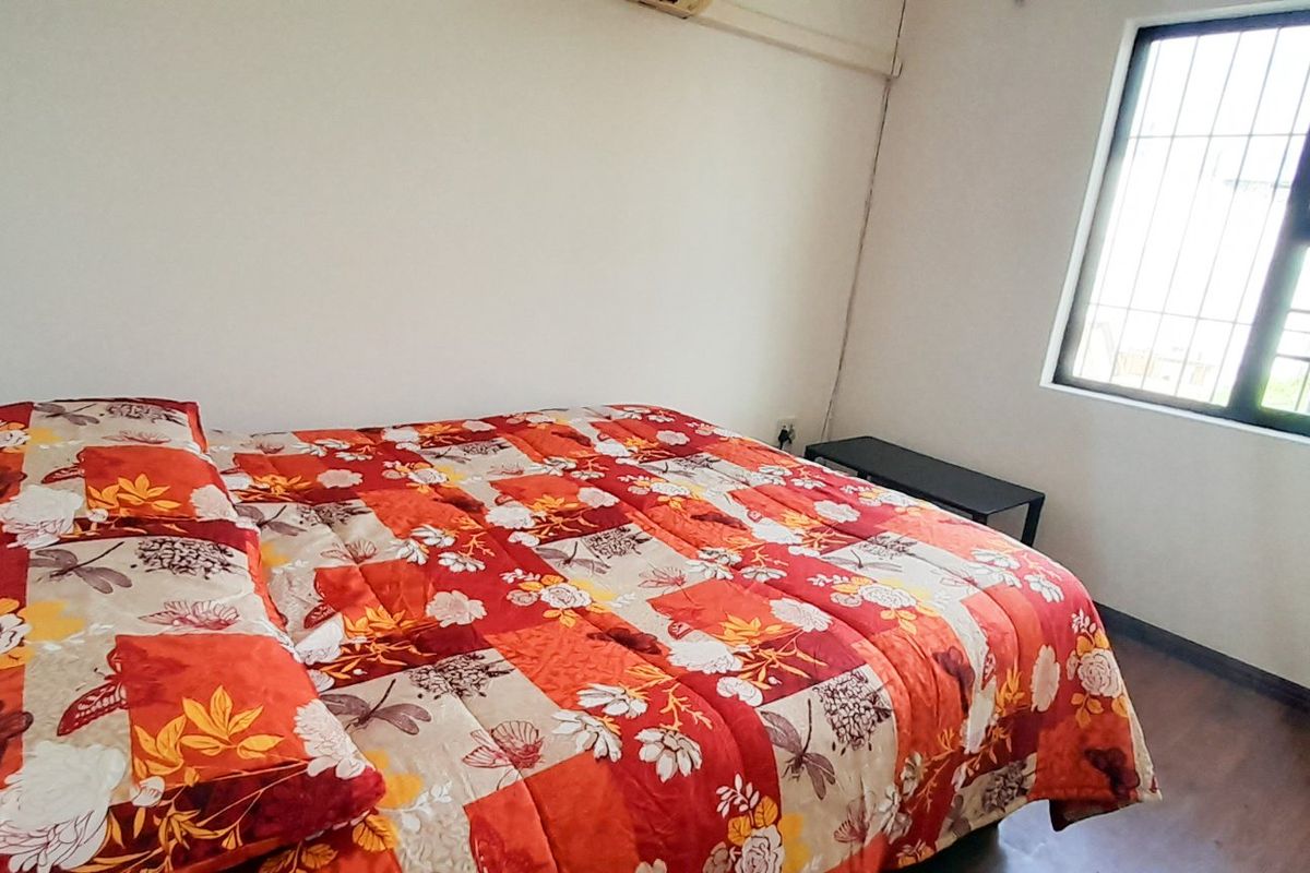 A functional bedroom featuring laminate flooring, a wall-mounted air conditioning unit, and a window fitted with security bars.