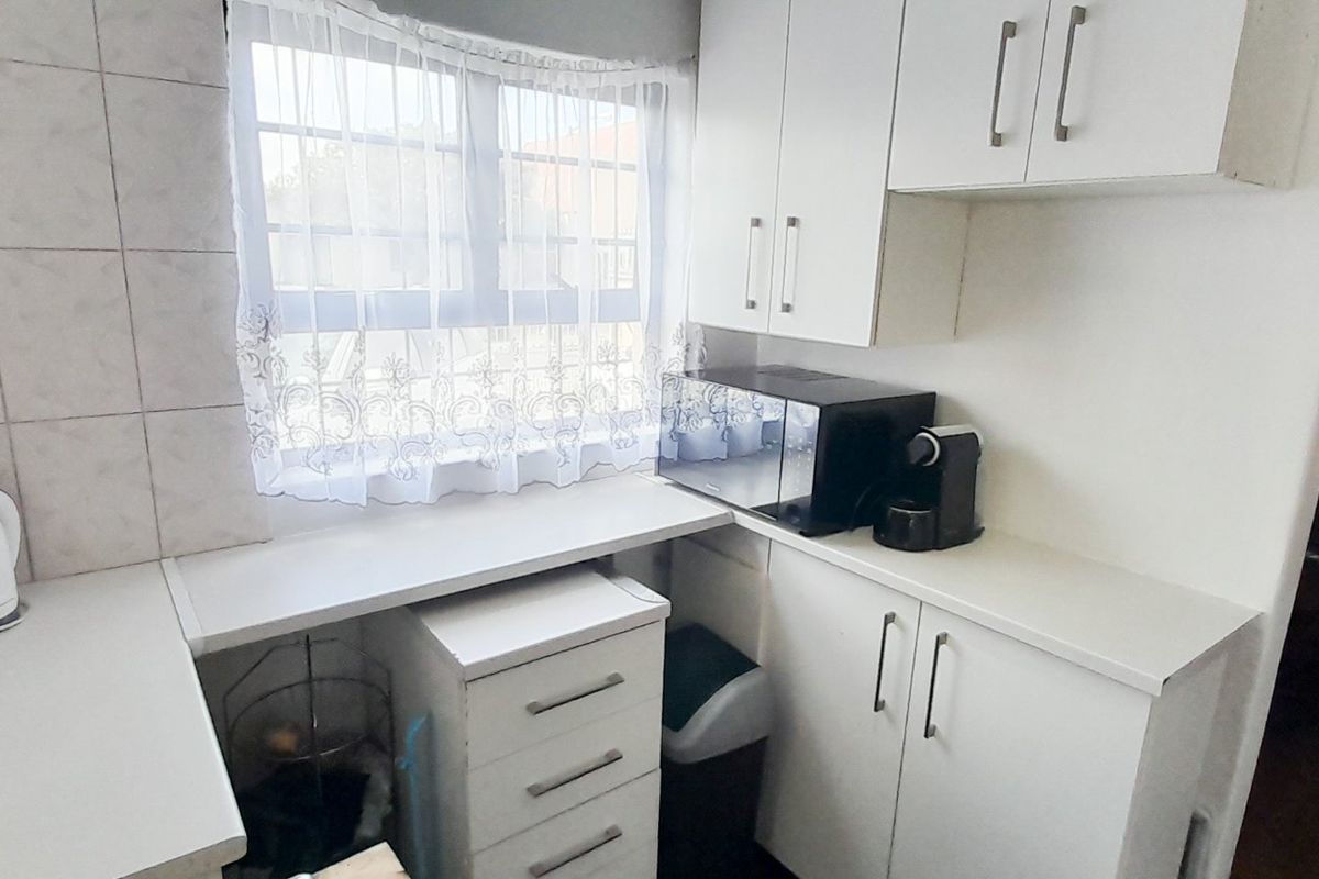 A compact kitchen area featuring white built-in cabinetry, laminate countertops, and a tiled splashback, providing functional storage and workspace.