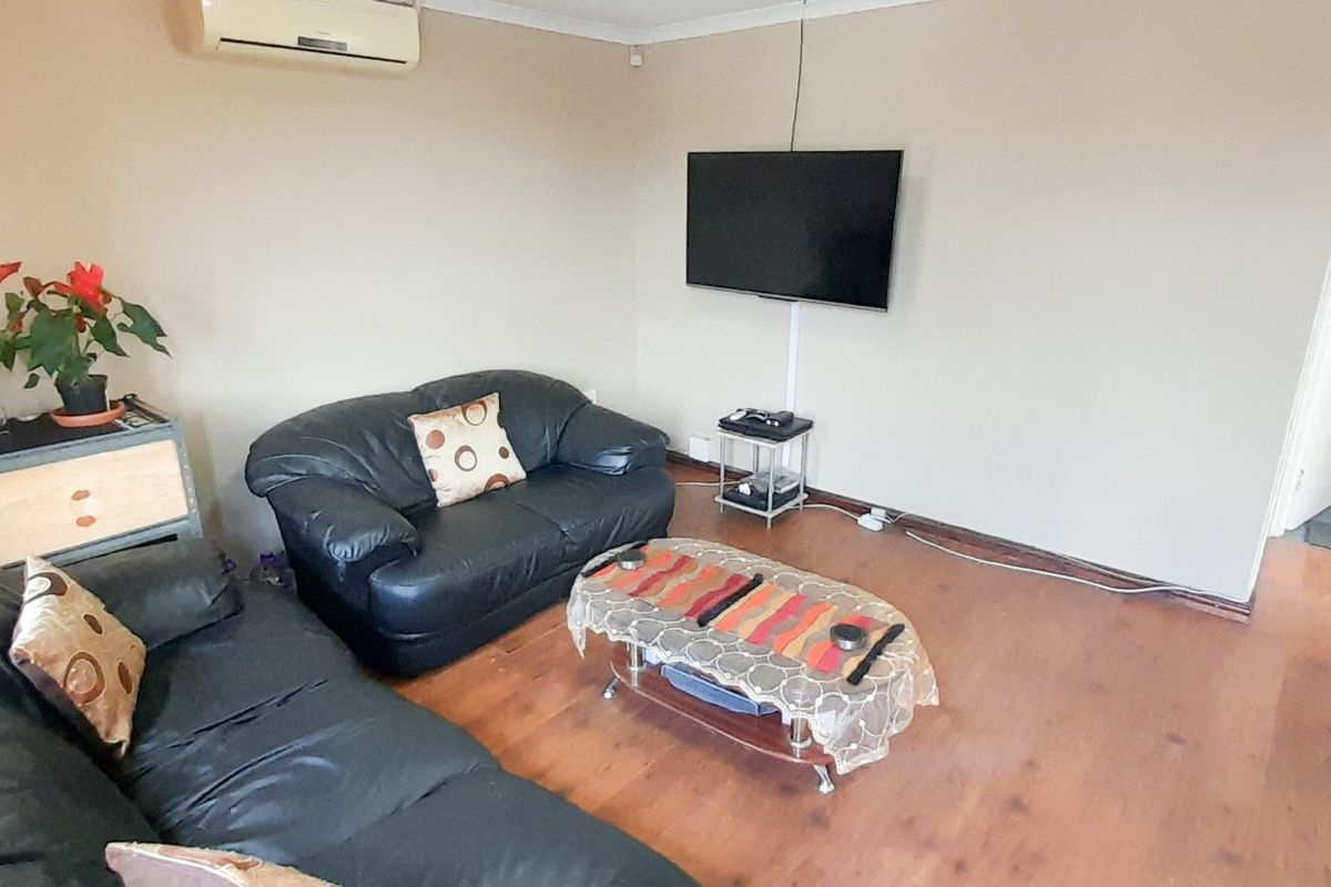 A living room featuring laminate flooring and a wall-mounted air conditioning unit, providing a functional space for relaxation.