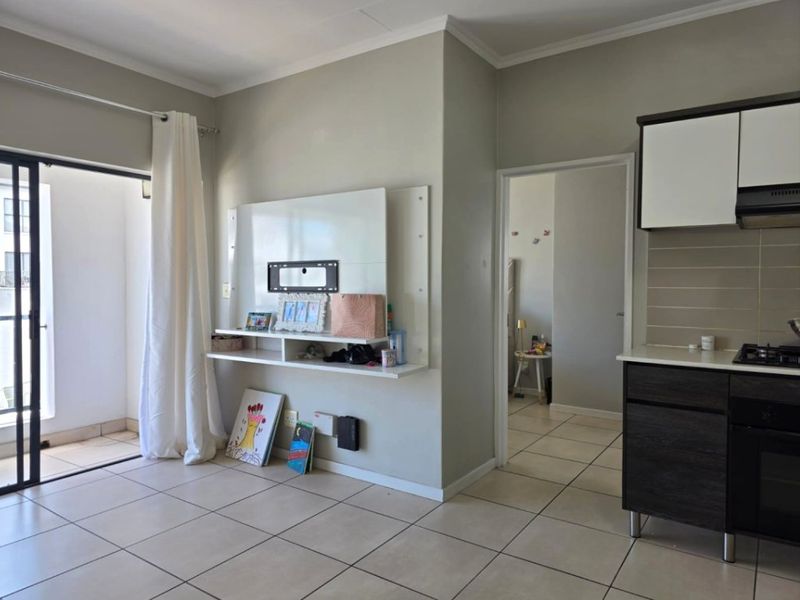 Open plan living area featuring tiled floors, a modern kitchen with built-in appliances, and direct access to a private balcony through sliding glass doors.
