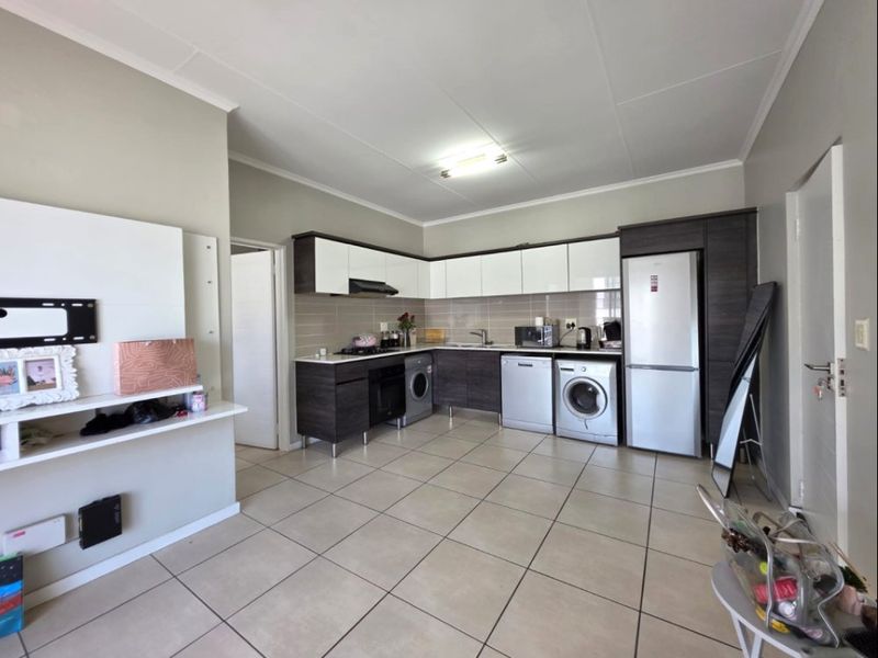 An open-plan living and kitchen area featuring modern two-tone cabinetry, tiled flooring, and integrated kitchen appliances.