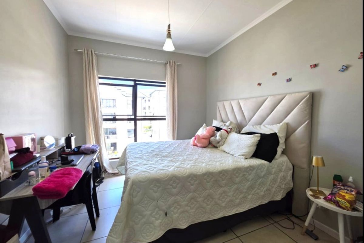 A well-lit bedroom featuring tiled flooring, a large window with natural light, and a neutral color palette.