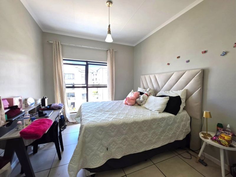 A well-lit bedroom featuring tiled flooring, a large window with natural light, and a neutral color palette.