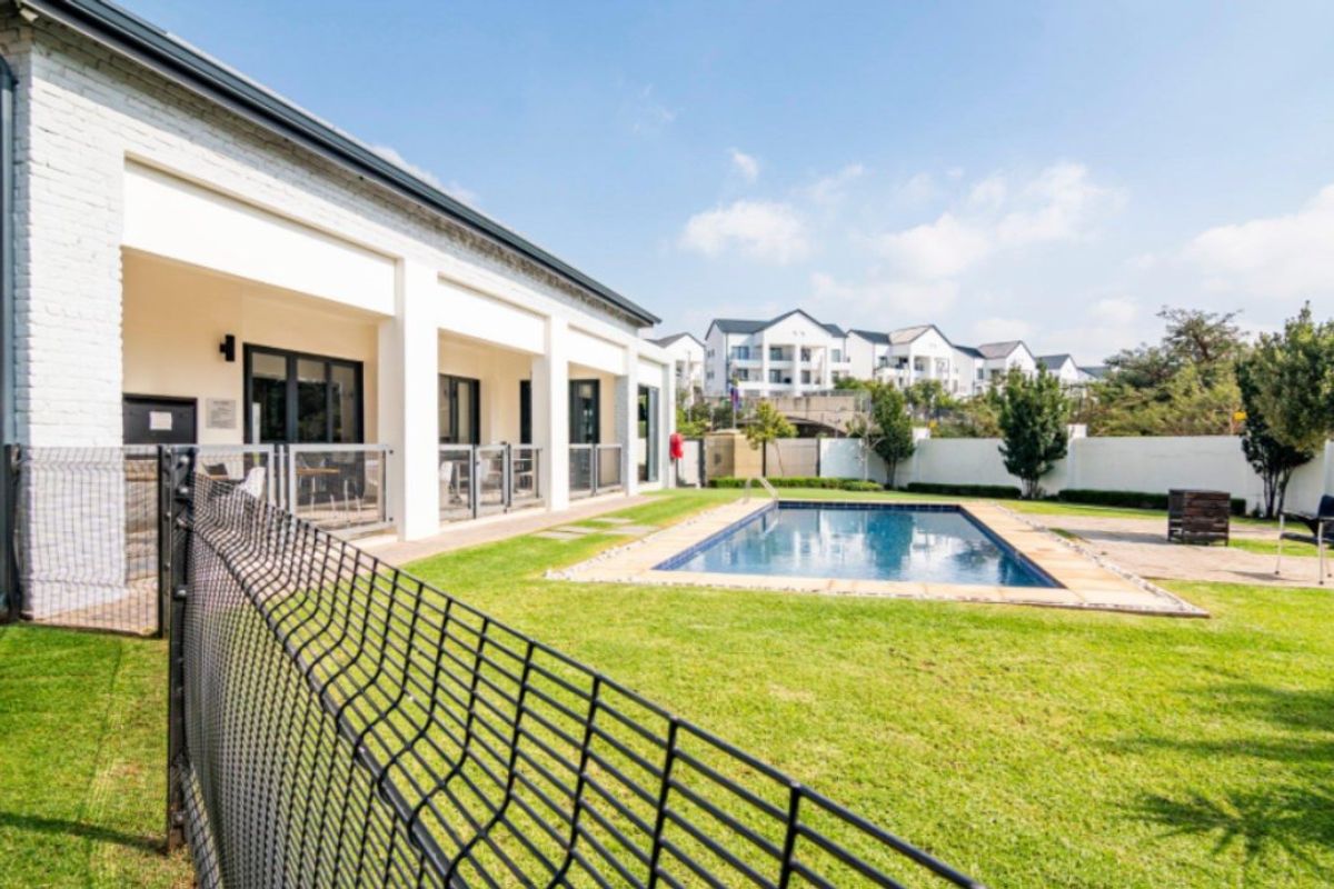 A well-maintained communal pool area featuring a swimming pool, manicured lawn, and a covered patio attached to the main building structure.