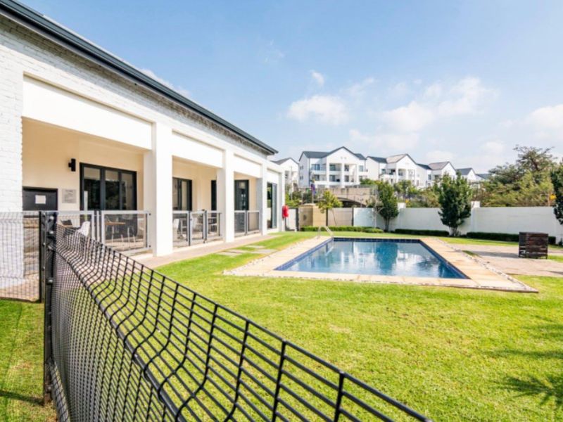 A well-maintained communal pool area featuring a swimming pool, manicured lawn, and a covered patio attached to the main building structure.