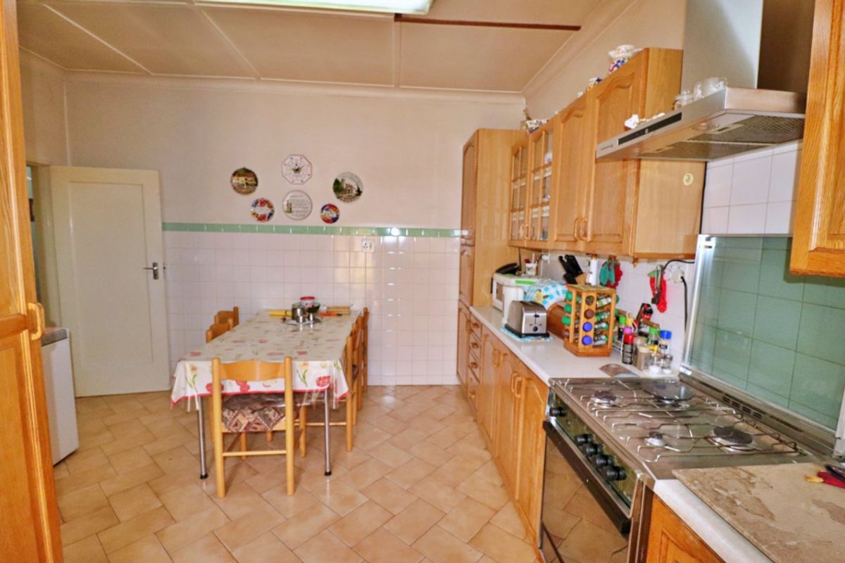 A functional kitchen featuring wooden cabinetry, a gas stove with extractor fan, and tiled splashbacks, offering a traditional layout with space for a dining table.