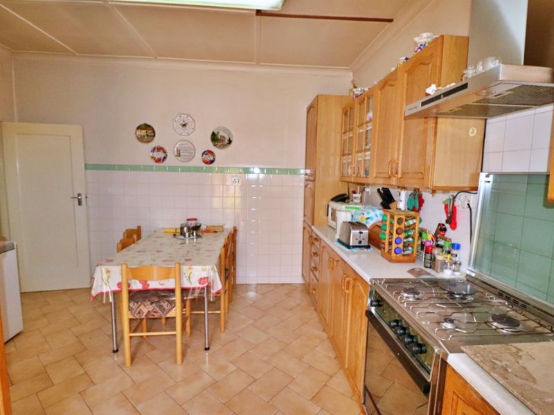 A functional kitchen featuring wooden cabinetry, a gas stove with extractor fan, and tiled splashbacks, offering a traditional layout with space for a dining table.