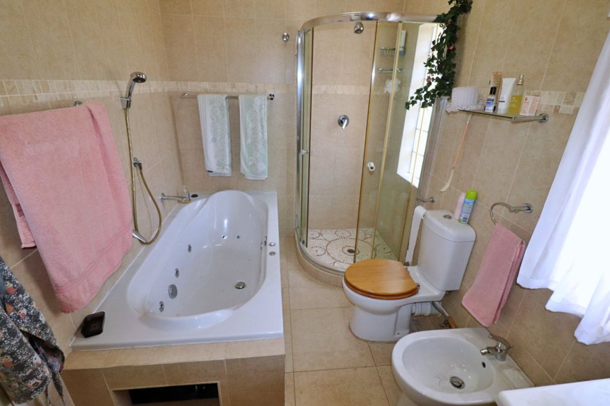 A functional bathroom featuring a built-in jetted bathtub, a corner shower enclosure, a toilet, and a bidet with neutral wall and floor tiling.