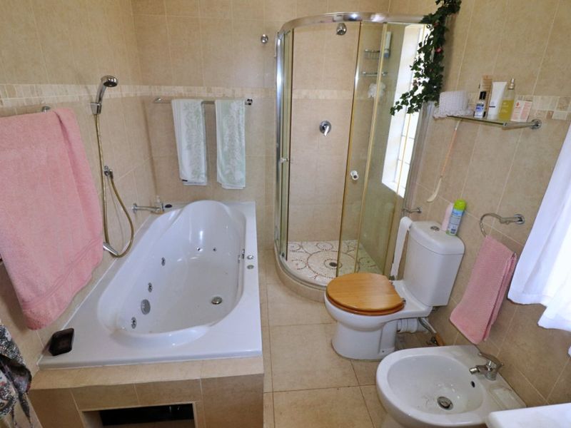 A functional bathroom featuring a built-in jetted bathtub, a corner shower enclosure, a toilet, and a bidet with neutral wall and floor tiling.