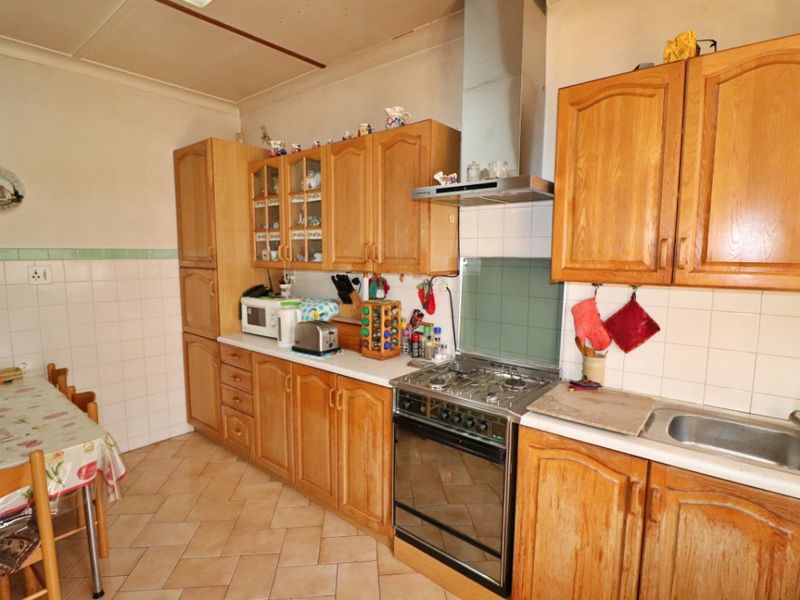 A functional kitchen featuring traditional wooden cabinetry, a gas stove with extractor fan, tiled backsplash, and durable tiled flooring.