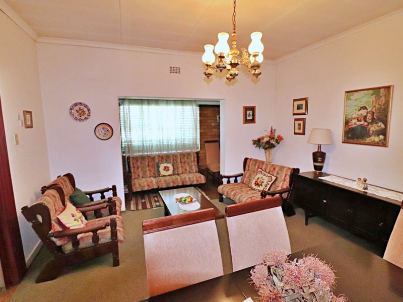 A traditional living room featuring a central chandelier, coved cornicing, and a brick feature wall, offering a classic layout with potential for modernization.
