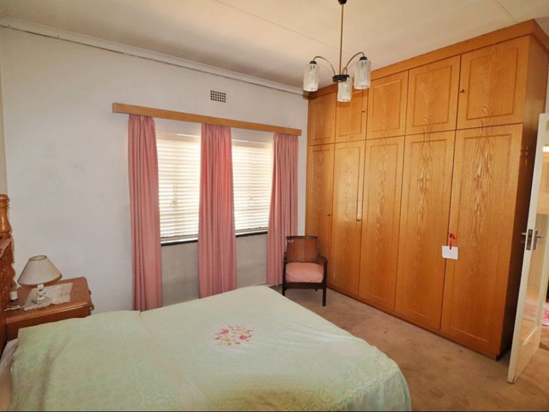 A bedroom featuring extensive built-in wooden cabinetry and a window with a wooden pelmet, offering a dated but functional living space.
