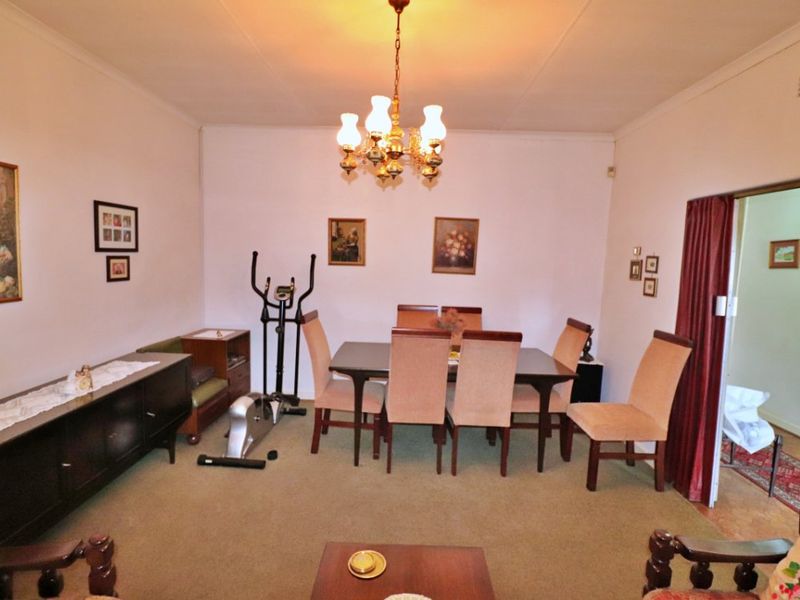 A traditional dining room featuring carpeted flooring, a central chandelier, and coved ceiling details, offering a functional space for family meals.