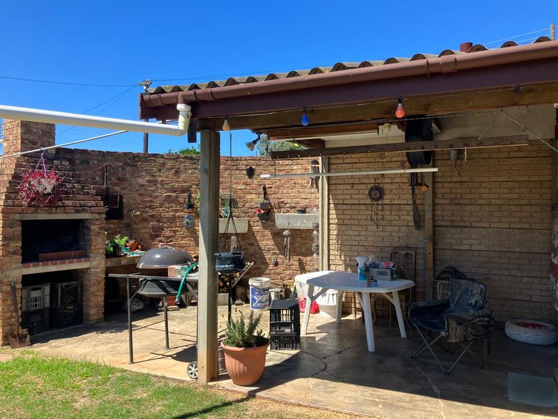Covered outdoor patio area featuring a built-in brick braai, concrete flooring, and a timber roof structure, offering potential for an enhanced entertainment space.
