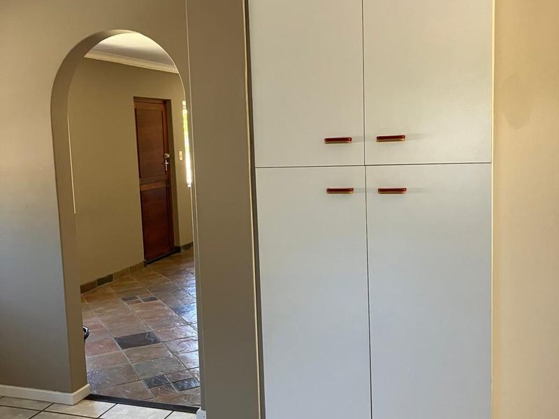 A clean hallway featuring neutral wall tones, tiled flooring, a built-in storage cupboard, and a classic architectural archway leading to an adjacent room.