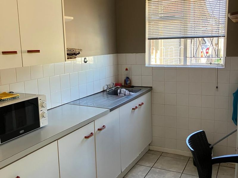 A functional kitchen featuring white built-in cabinetry, a stainless steel sink, tiled splashbacks, and tiled flooring, offering a clean and practical workspace.