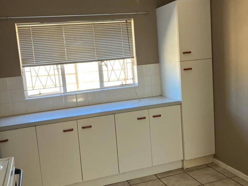 A functional kitchen area featuring white built-in cabinetry, tiled flooring, and a tiled splashback, offering a clean and practical space for culinary activities.
