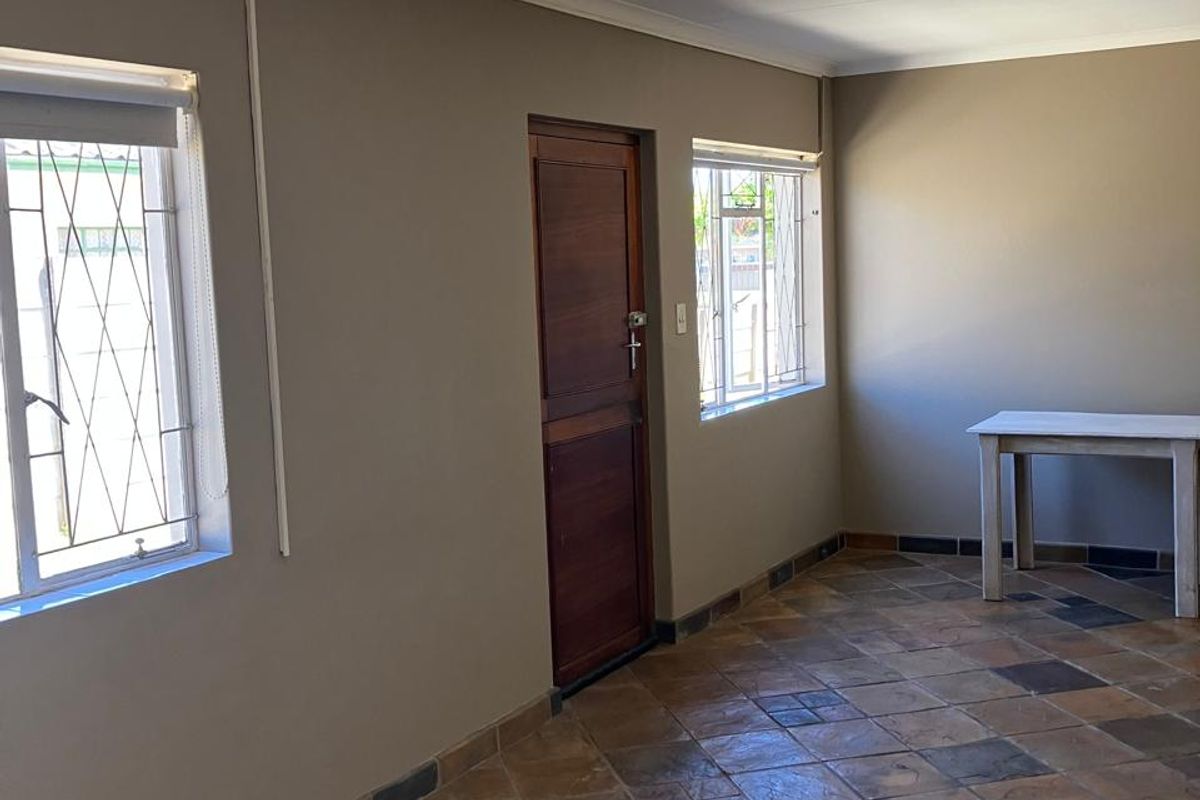An empty living area featuring tiled flooring, neutral wall tones, and security bars on the windows, providing a clean and functional space.