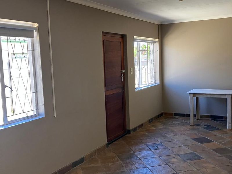 An empty living area featuring tiled flooring, neutral wall tones, and security bars on the windows, providing a clean and functional space.
