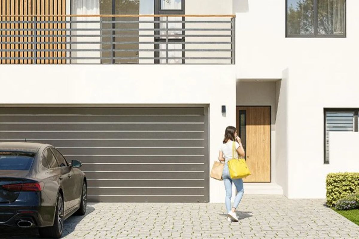 Modern front facade featuring a paved driveway, sectional garage door, timber entrance door, and an upper-level balcony with metal railings.