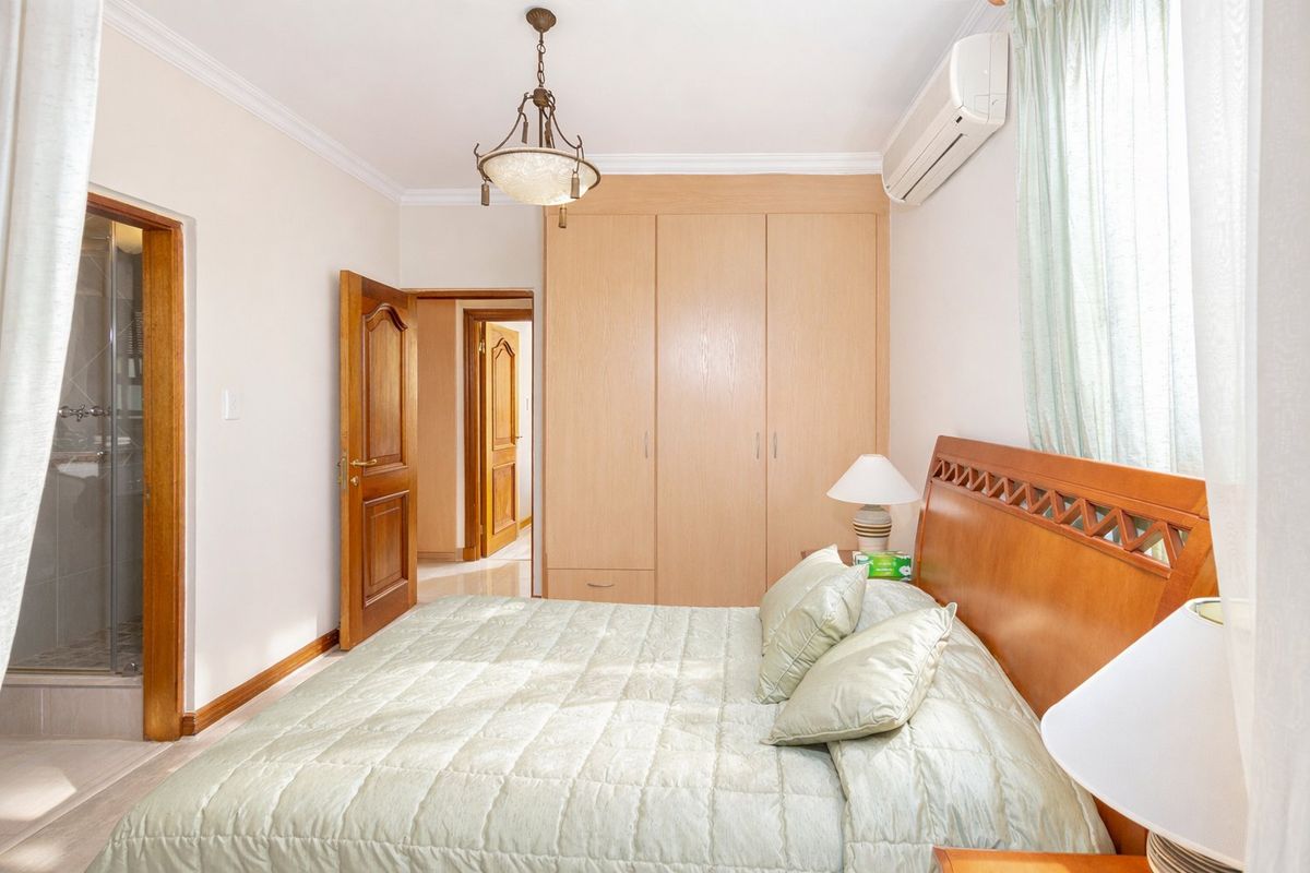 A well-maintained bedroom featuring built-in wooden wardrobes, split-system air conditioning, and direct access to an en-suite bathroom.