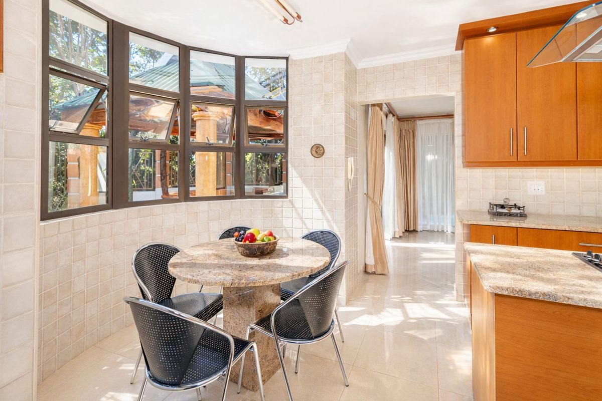 A bright kitchen featuring wooden cabinetry, granite countertops, tiled finishes, and a large bay window overlooking the outdoor area.