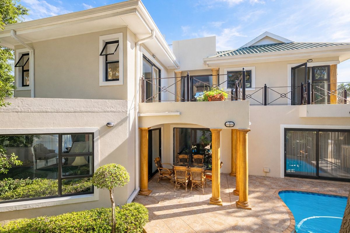 Rear view of the house featuring a tiled patio area, swimming pool, upper balcony with metal railings, and decorative columns.