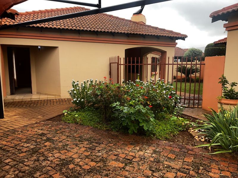 Front exterior view of a townhouse featuring a paved driveway, covered entrance, and terracotta roof tiles with established garden beds.