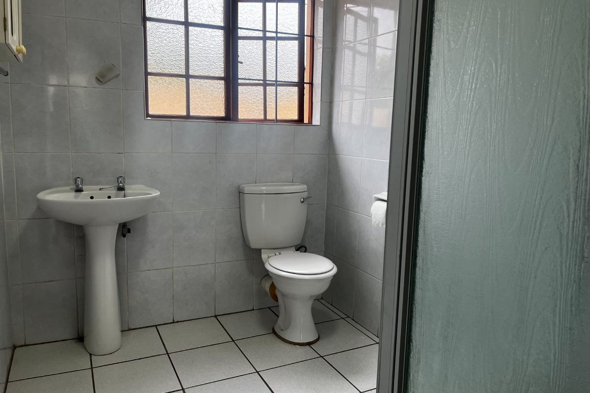 A functional bathroom featuring a pedestal basin, toilet, and tiled finishes, offering a clean space ready for potential modernization.