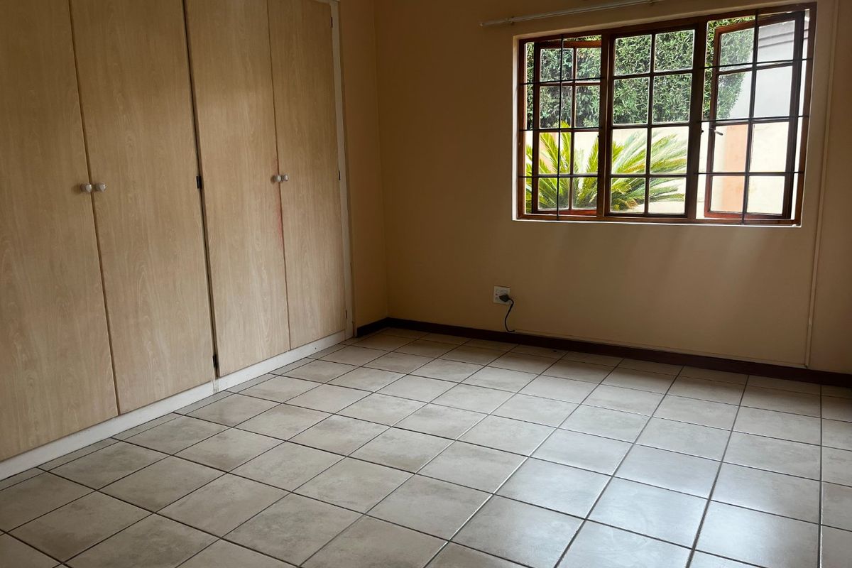 An empty bedroom featuring tiled flooring, built-in cupboards, and a wall-mounted air conditioning unit, providing a functional and neutral space.
