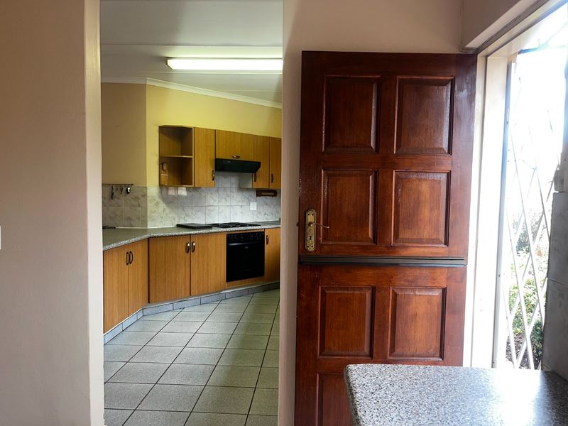 A functional kitchen featuring built-in wooden cabinetry, laminate countertops, a built-in oven with hob, and tiled flooring, viewed through a wooden doorway.