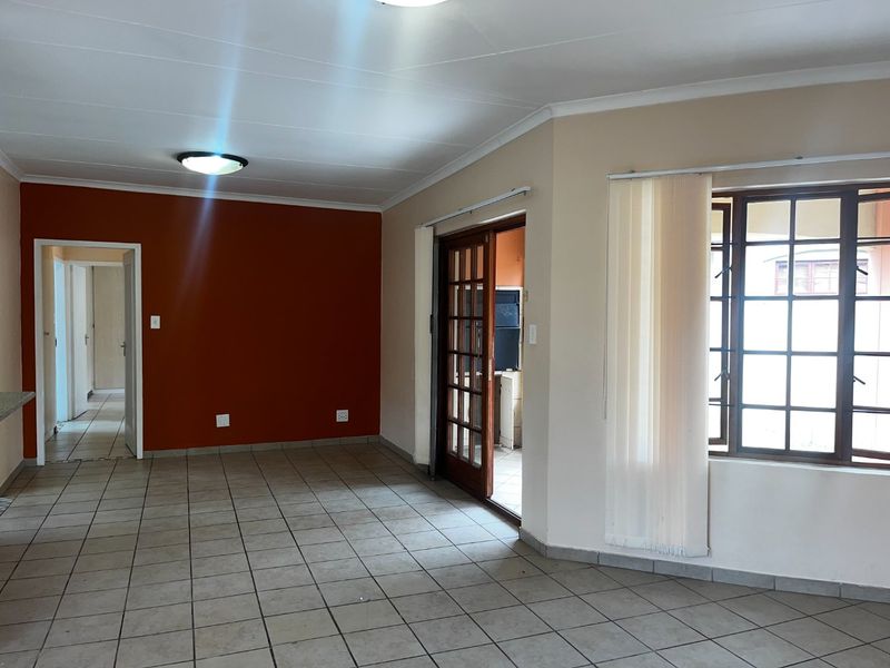 An empty living room featuring tiled flooring, a wooden framed glass door leading to an adjacent space, and a large window with vertical blinds.
