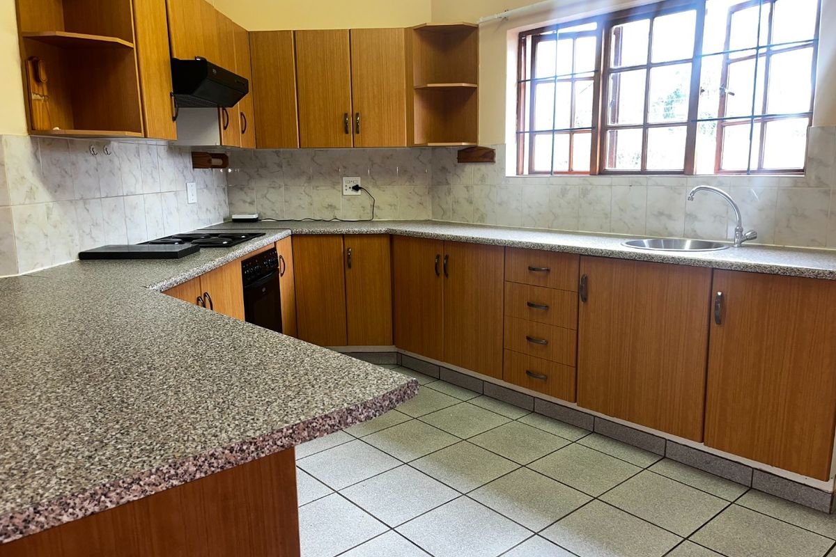 A functional kitchen featuring wood-look laminate cabinetry, granite-style countertops, built-in cooking appliances, and tiled flooring with ample natural light from the casement windows.