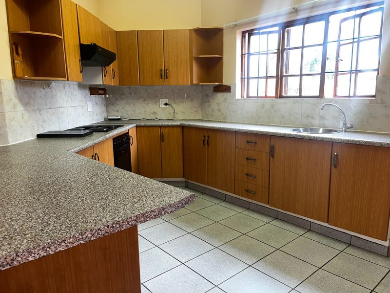 A functional kitchen featuring wood-look laminate cabinetry, granite-style countertops, built-in cooking appliances, and tiled flooring with ample natural light from the casement windows.
