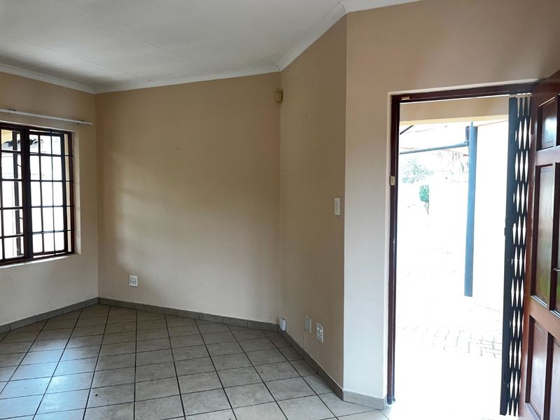 An empty living room featuring tiled flooring, a security gate at the entrance, and a window fitted with burglar bars.