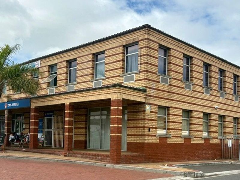 A two-story commercial building featuring a distinctive two-tone brick facade, a covered entrance area, and paved street-level access.